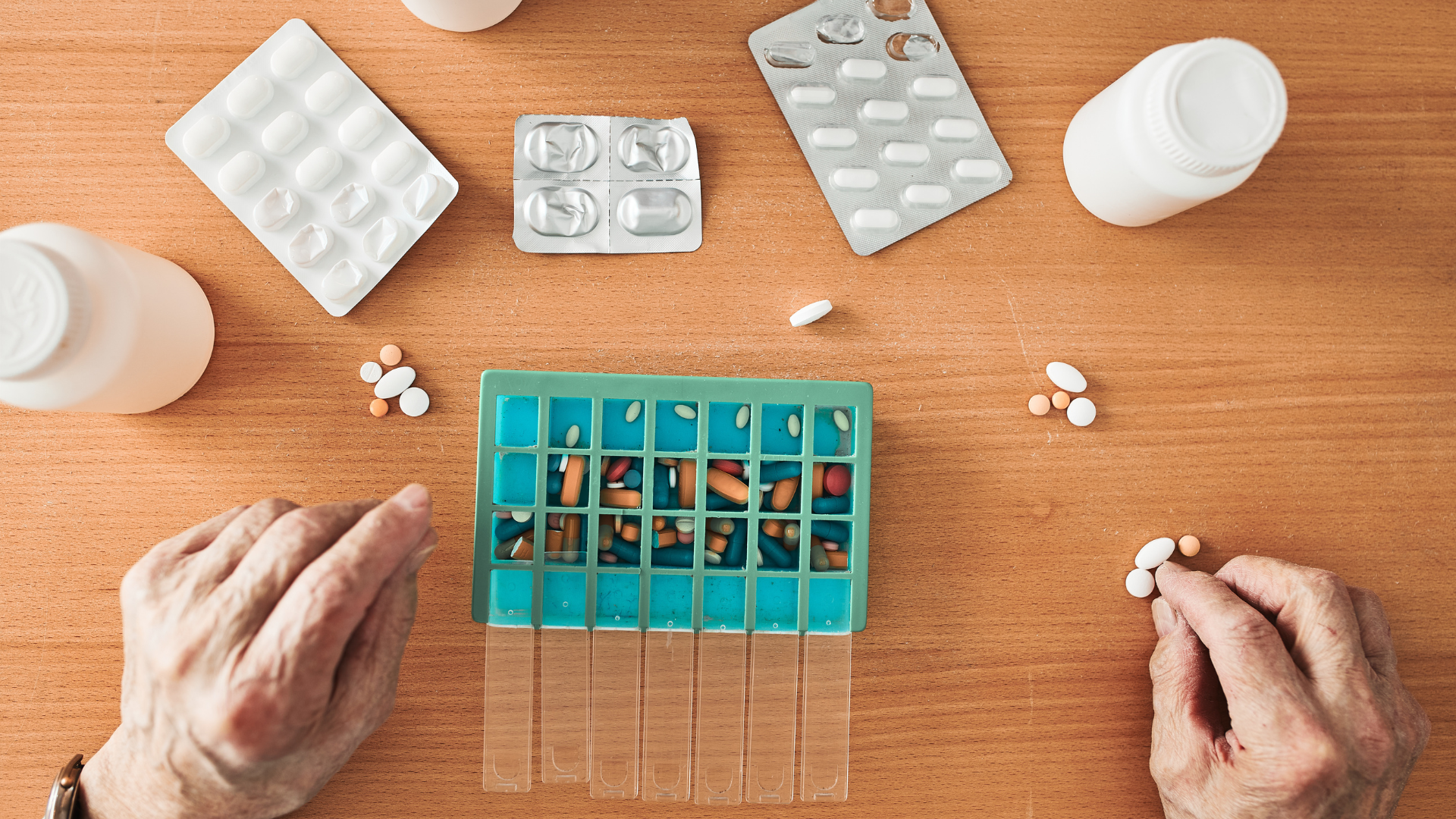 An older person organizes their medications amidst medication bottles and medication blister packs