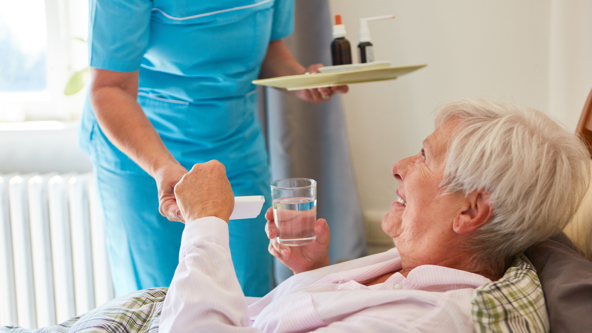 Long-term care resident happily accepts medication from a staff member who ensures her medication adherence